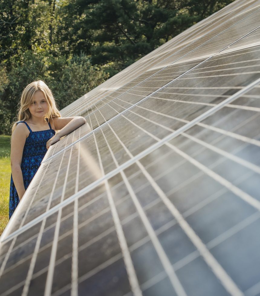 A young girl standing beside and leaning against a large solar panel installation.